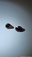 Two faceted sapphires, one orange and pear-shaped, the other pink and oval-shaped, displayed on a white background.