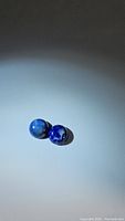 Two round deep blue lapis lazuli cabochon stones placed on a light colored surface, showing color and size match.
