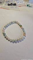 Image showing the full round bracelet with pastel colored gemstone beads laid on a white background with various small gem bags in the background.