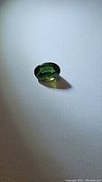 Natural green sapphire gemstone lying flat on a white surface, showing its oval cut, color, and brilliance.