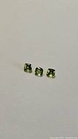 Three apple green natural peridot gemstones in cushion cut, arranged on a white surface.