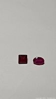 Two natural rubies on flat surface, showing shape and color under normal light.