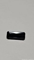 Rectangular cut Paraiba blue tourmaline gemstone photographed on white/light background showing color and facet detail.