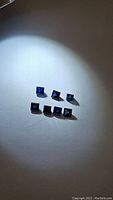 Seven square-cut royal blue sapphires arranged on a white background under spotlight, showing their deep blue color and faceted cuts.