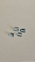 Four emerald cut sky blue topaz gemstones on beige background showing clarity and color