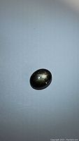 Black star sapphire gemstone on plain white background showing star effect on polished dome surface.