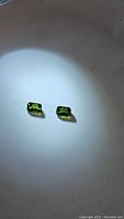 Pair of small rectangular emerald cut green tourmaline gemstones positioned under a focused light source showing vibrant green color and good clarity.