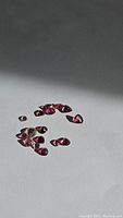 Multiple untreated pink tourmaline stones scattered on a white background showing various sizes and teardrop shapes.