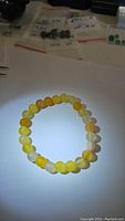 Top view of round yellow agate bead bracelet laid flat on white surface. Various yellow hues and translucent beads visible.