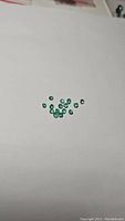 Photo showing multiple small, round, green Zambian emerald gemstones against a plain white background.
