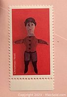 Front of stamp showing red Christmas doll design and perforations. Missing country name, denomination and tagging.