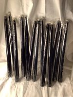 Thirteen black taper candles wrapped in plastic, displayed on a surface.