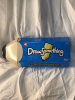 Top and side views of the sealed Draw Something board game box showing branding, age rating, and bilingual description.
