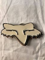 Front view of vintage Fox Racing belt buckle showing iconic stylized fox head logo with chrome and white enamel