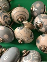 Close-up of various blue and white ceramic knobs with metal screw fittings arranged on a green surface