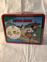 Front view of the tin lunch box showing Mickey Mouse and friends and sealed sticker with candy details.