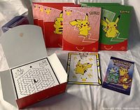 Three McDonald's promotional Pokémon card boxes (red, pink, green) shown closed and one open revealing maze puzzle inside lid, with unopened Pokémon trading card booster pack and Pikachu promotional cards on white background.