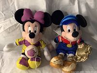 Both Mickey and Minnie Mouse plush toys shown together, highlighting heavy tarnish and discoloration on Mickey's right arm and both shoes.