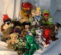 Full lot of mixed vintage plush toys arranged on light sheet backdrop showing various character plush including Disney and animals.