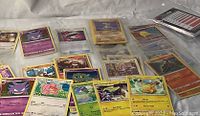Photo showing various Pokémon cards spread on a white cloth including Gengar, Slowpoke, Maractus, Galvantula, Pikachu