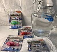 Four sealed robot fish toys in original packaging, each with batteries included. Displayed next to water pitcher and blue fish (not included).
