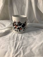 White ceramic mug with cartoon cow design on the front and sides. Glossy surface, large handle visible.