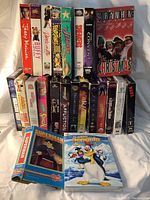 Photo showing a stacked collection of various VHS tapes including Saturday Night Live Christmas Special, My Girl, Alvin, G.I. Jane, Buffy the Vampire Slayer, The Flintstones, The Jetsons among others.