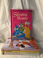 Five hardcover Walt Disney books stacked with Sleeping Beauty on top showing bright pink cover and fairy characters.