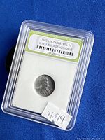 Photo of a 1943 Lincoln Steel 1 cent coin in a protective plastic case labeled by the International Numismatic Bureau as 'W.W.II Emergency Issue'. The label and coin are clearly visible.