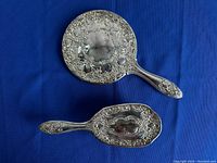 Top view of silver plated hair brush and hand mirror showing ornate floral and scroll embossed design on backs and handles.