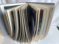 View of the binder partially open showing thick collection of photo pages inside clear plastic sleeves.