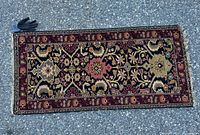 Full view of rectangular Persian rug laid flat on asphalt, showing its color and pattern details with a glove for size reference.