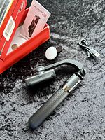 Folded handheld black gimbal stabilizer with detachable spherical white light, USB charging cable, user manual and red box on gray carpet.