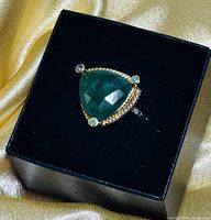 Top-down view of ring on black cushion showing triangular emerald and accent stones