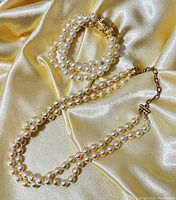 Photo of double strand pearl necklace and matching bracelet laid on silky yellow fabric showing clasp details and pearl finish.