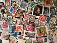 Close-up photo showing a pile of assorted international postage stamps in various colors, sizes, and designs, mostly used without hinges.