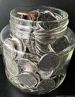 Glass jar filled with a large quantity of Canadian coins, mostly nickels, some pennies.