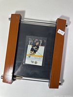 Framed hockey card with Bobby Orr in Boston Bruins uniform and signature on card, mounted on black matte background, wood and metal frame.