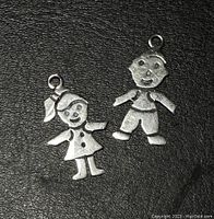 Front view of two silver child-shaped pendants on a black background showing design details