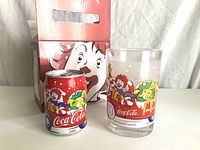 Glass and soda can with vintage McDonald's and Coca-Cola Christmas design placed side by side with their box showing Ronald McDonald illustration.