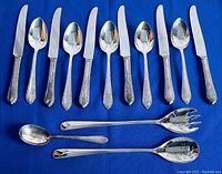 Top view of silver-plated cutlery for six with knives, tablespoons, teaspoons, and forks arranged on blue fabric.