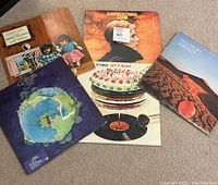 All five vinyl records displayed together on the floor, showing front covers including David Bowie Low with sticker and marking, Rolling Stones Let It Bleed, Yes Fragile, The Nice Elegy, and Pussy Cats album covers.