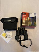 Photo showing binoculars, carrying case, lens cloth, instruction manual, and original Bushnell product box.