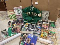 Full view of lot including Celtics jacket and various Celtics memorabilia magazines, books and collectible prints arranged on the floor.