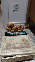 View of the dragon figurine alongside the decorative jewelry box on the carpet.