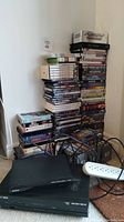 Photo showing Sony DVD player, Cisco NextBox digital box, large stack of DVDs and VHS tapes, extension cords and cables on the floor