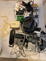 Lot of electronics with VTech cordless phones, Sony cassette player, GE clock radio, Olympus digital camera, and Dora flip cell phones all shown mixed with charging cables and accessories.