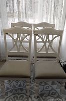 Four white slate back side chairs with beige linen seats arranged in two rows, showing front views with starry curtains in the background