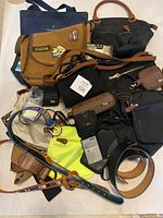 Overview of handbags, wallets, calculator, eyeglass cases, lanyard, and belts arranged on a surface.