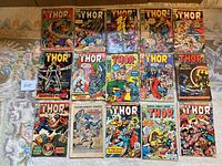Top view of 15 assorted Marvel Thor comic books arranged in a grid on the floor, showcasing colorful front covers with various characters and titles.